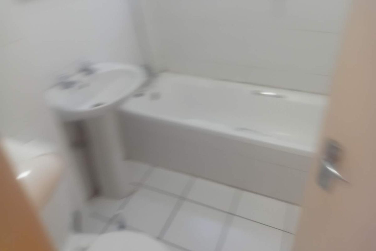 A functional bathroom featuring a pedestal basin, bathtub, and toilet with tiled finishes.