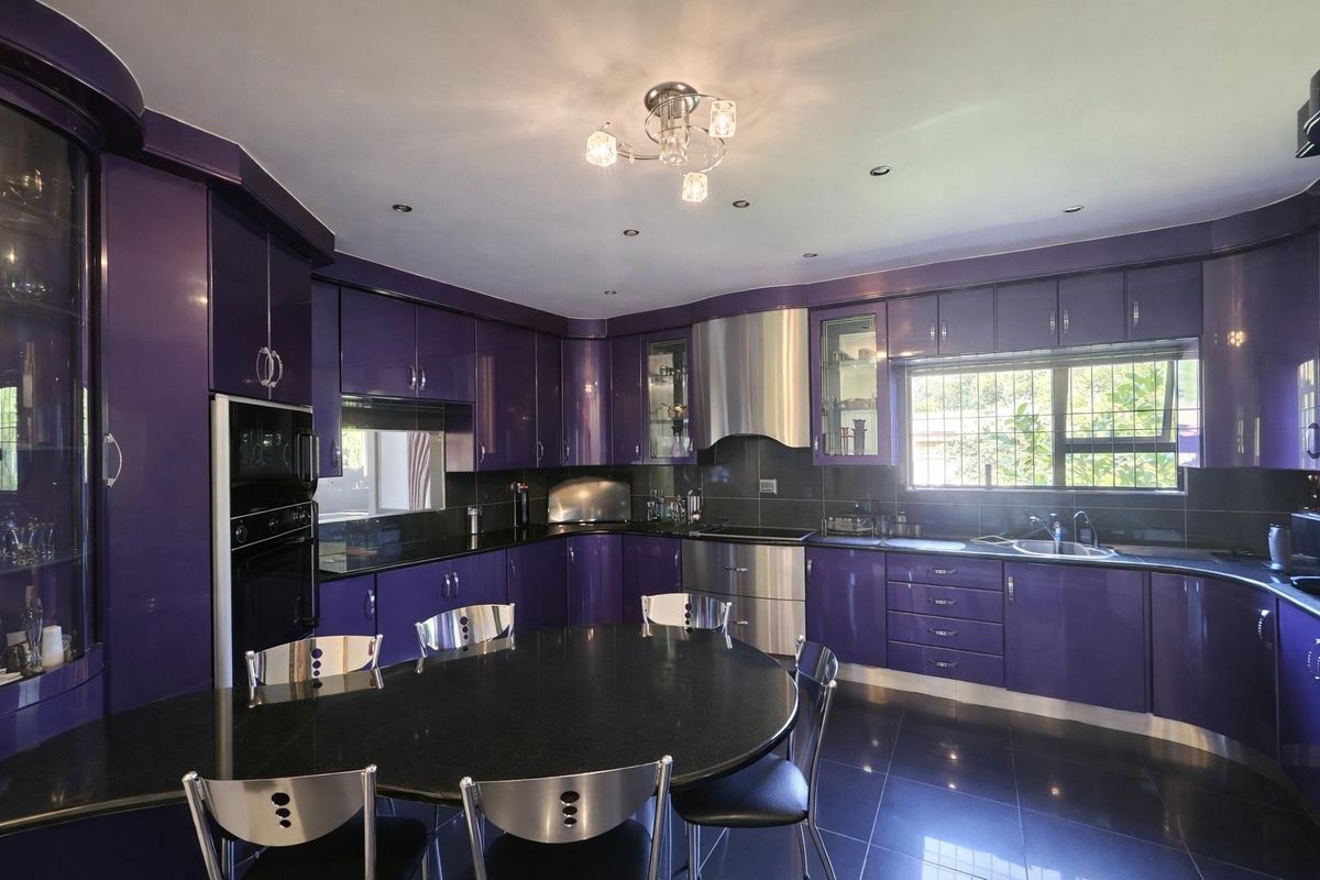 A spacious kitchen featuring high-gloss purple cabinetry, black granite countertops, stainless steel appliances, and integrated lighting.
