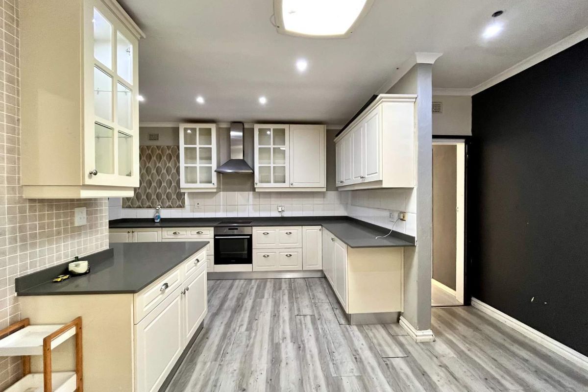 A spacious kitchen featuring white cabinetry, dark stone countertops, integrated oven, extractor fan, and modern laminate flooring with a neutral tiled backsplash.