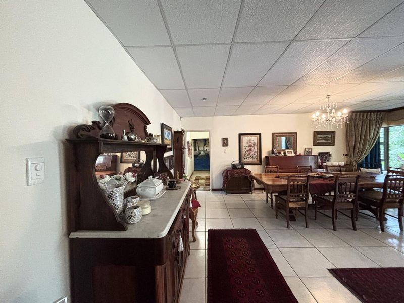 Spacious open-plan living and dining area featuring tiled flooring, a drop ceiling, and a classic chandelier, offering a versatile layout for family gatherings.