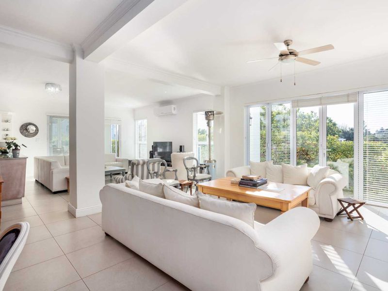 Spacious open-plan living area featuring neutral tiled floors, ceiling fan, air conditioning, and large glass doors providing ample natural light and garden access.
