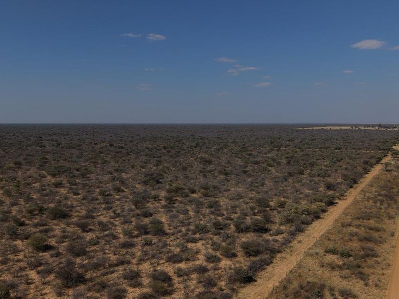 An aerial view of a vast, undeveloped farm landscape featuring a long dirt road and perimeter fencing under a clear sky.
