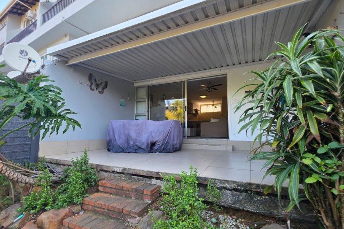 A covered patio area featuring tiled flooring and sliding glass doors leading into the main living space, with brick steps providing garden access.