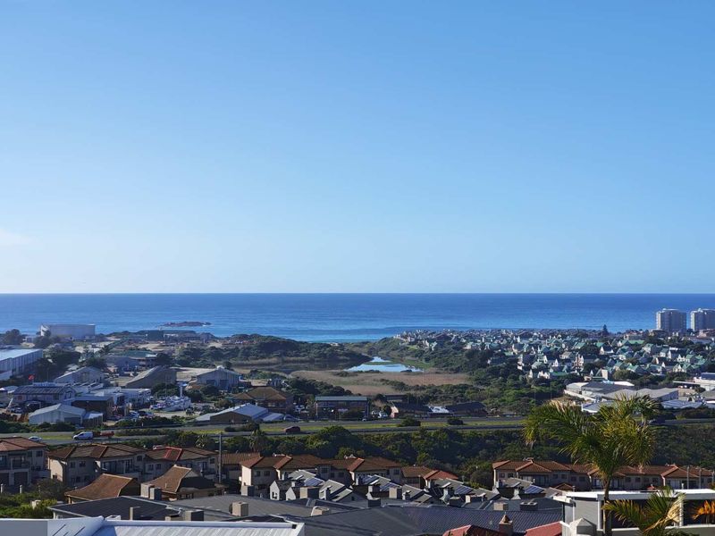 A wide-angle elevated view overlooking the coastal landscape, residential neighborhood, and the ocean horizon.