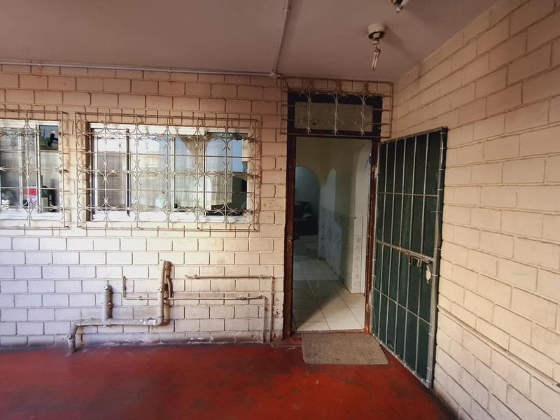 An empty utility or service area featuring exposed brick walls, security bars on windows, and visible plumbing infrastructure.