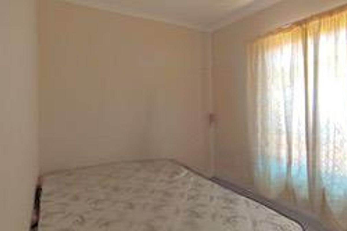 A simple bedroom featuring neutral walls, a window with curtains, and a mattress.