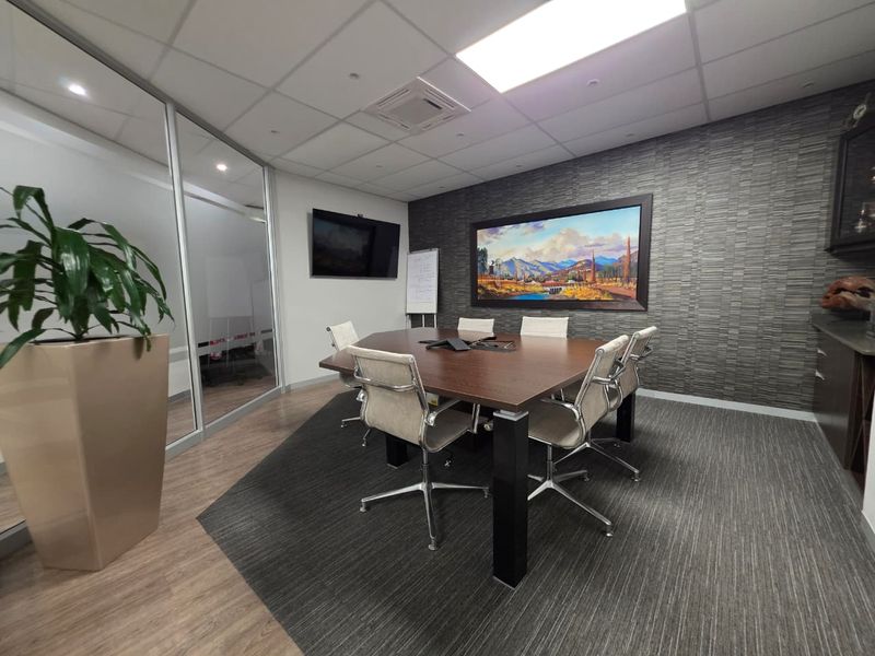 A professional meeting room featuring a glass partition, textured feature wall, suspended ceiling, and integrated cabinetry.