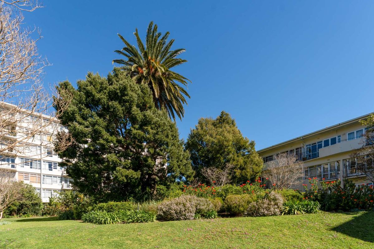 A view of the apartment complex exterior featuring a well-maintained communal garden with mature trees and established landscaping.
