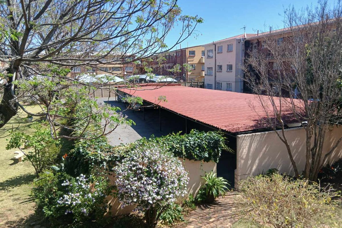 An elevated view of the apartment complex rear area, featuring a covered carport, paved pathways, and established garden landscaping.