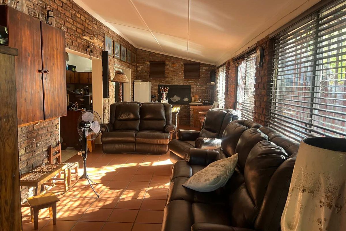 Spacious living room featuring exposed brick walls, tiled flooring, and a sloped ceiling with natural light filtering through venetian blinds.