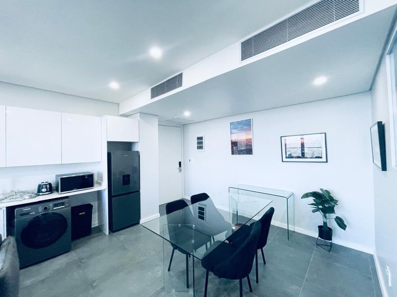 Modern open-plan living and kitchen area featuring sleek white cabinetry, ducted air conditioning, and contemporary tiled flooring in a well-maintained apartment setting.