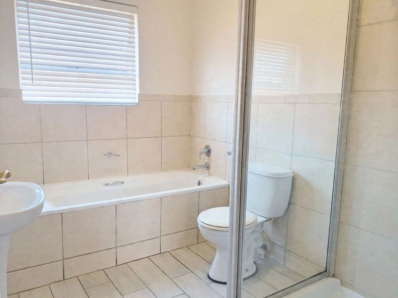 A clean and functional bathroom featuring a bathtub, separate shower enclosure, pedestal basin, and neutral wall and floor tiling.