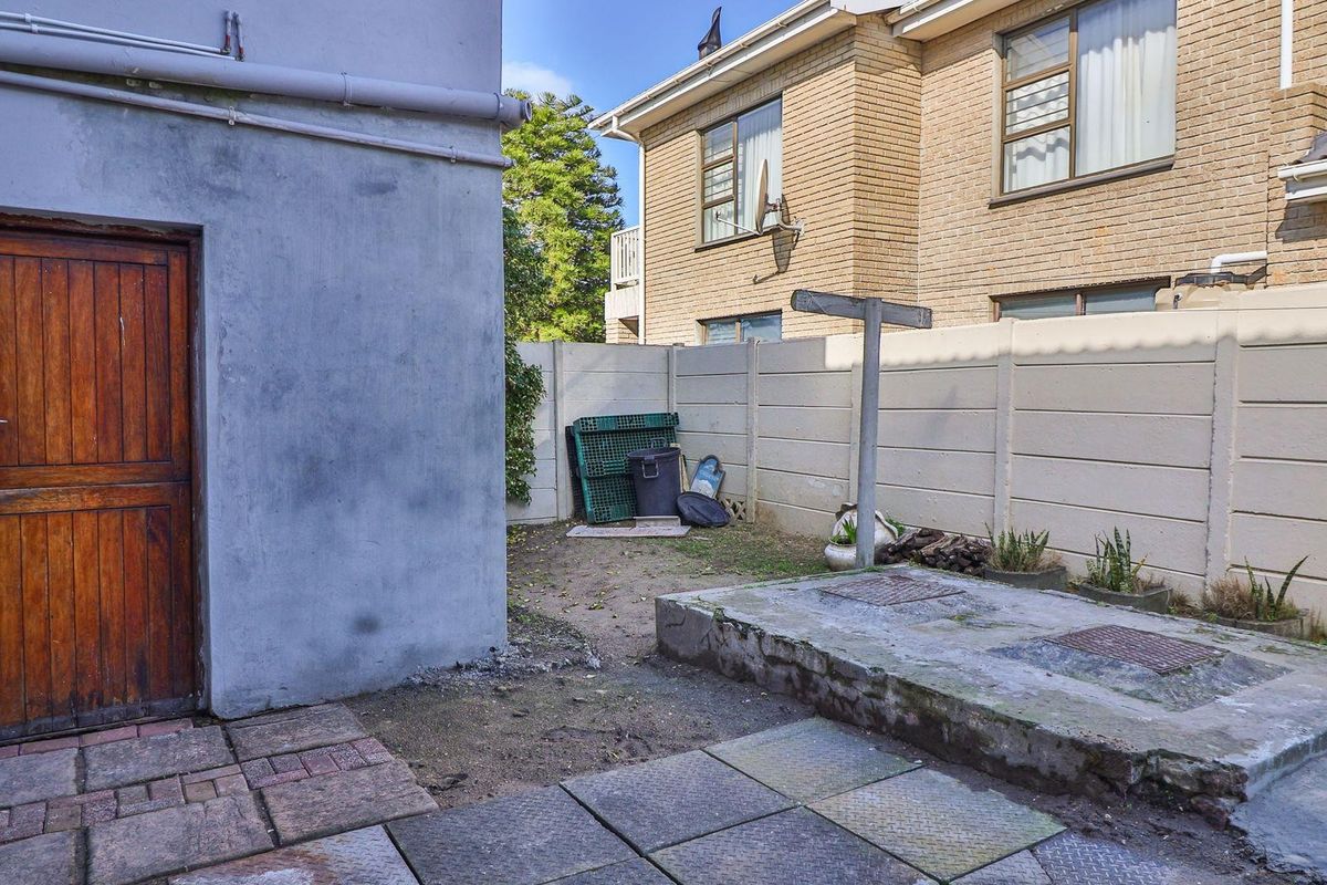 A rear exterior area featuring a concrete platform, paved section, and perimeter walling, providing a functional utility space with potential for landscaping improvements.