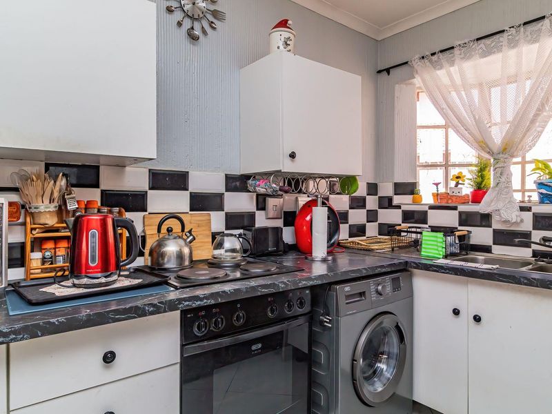A functional kitchen featuring built-in cabinetry, a dark laminate countertop, electric hob, built-in oven, and a stainless steel sink with a tiled backsplash.