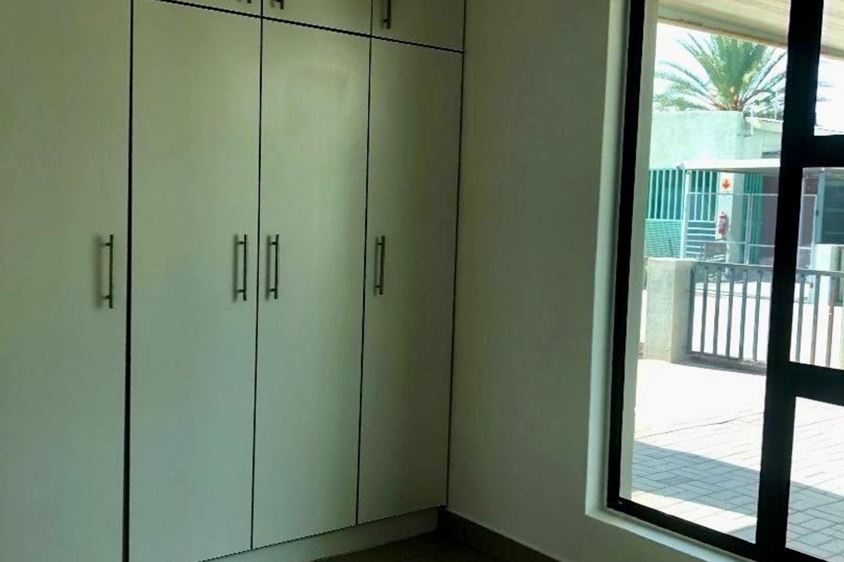 A clean, empty bedroom featuring neutral tiled flooring and extensive floor-to-ceiling built-in cupboards, offering ample storage space.