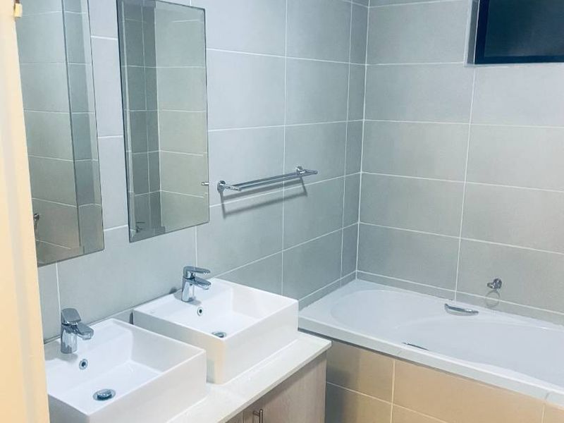 A clean, modern bathroom featuring a double vanity with vessel sinks, built-in bathtub, and neutral wall and floor tiling.