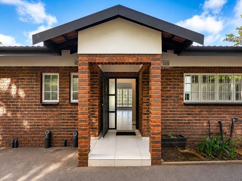 Front entrance of a townhouse featuring an exposed brick facade, tiled porch, and secure entry door with views through to the interior.