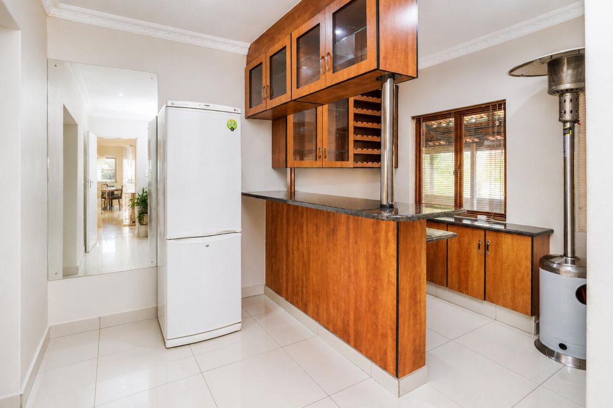 A functional kitchen area featuring wooden cabinetry, granite countertops, and tiled flooring, offering a practical layout with integrated storage and a breakfast bar.