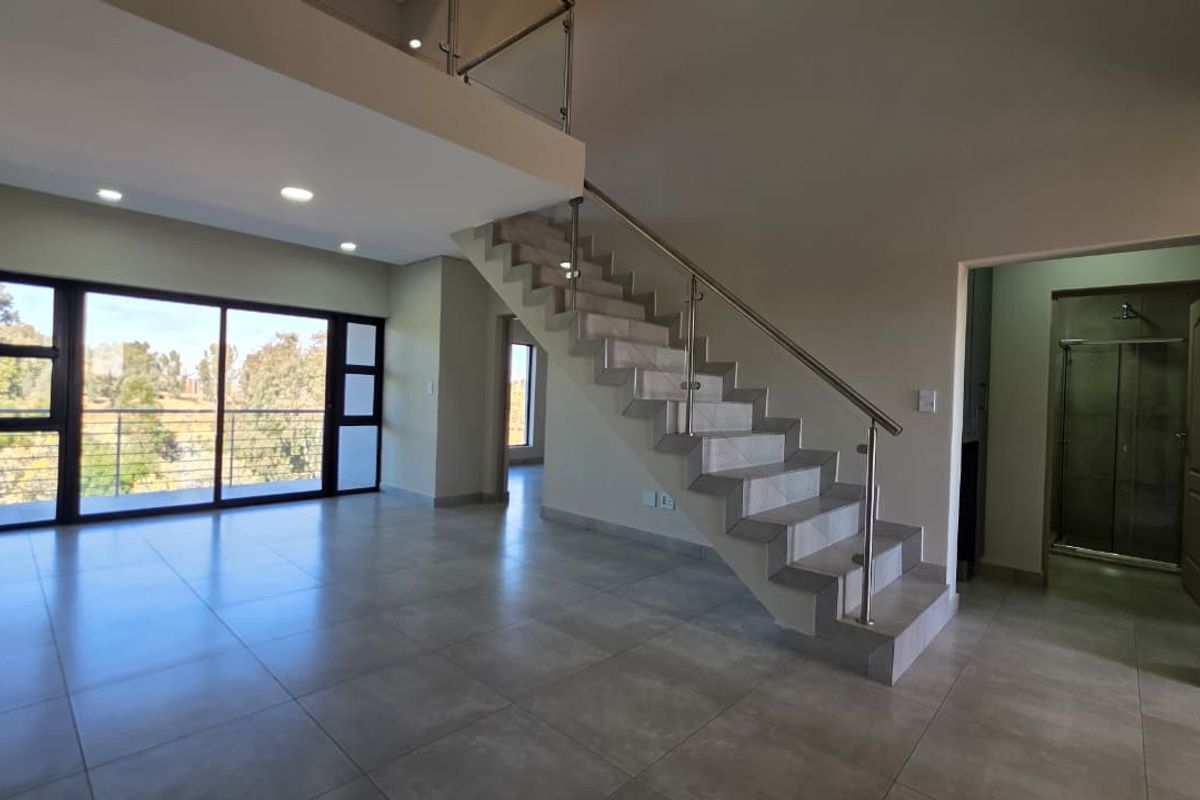 Spacious open-plan living area featuring modern tiled flooring, a sleek staircase with glass balustrades, and large sliding doors leading to a balcony.