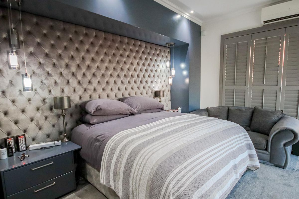 A well-appointed bedroom featuring a large tufted upholstered headboard, integrated recessed lighting, and plantation-style shutters.