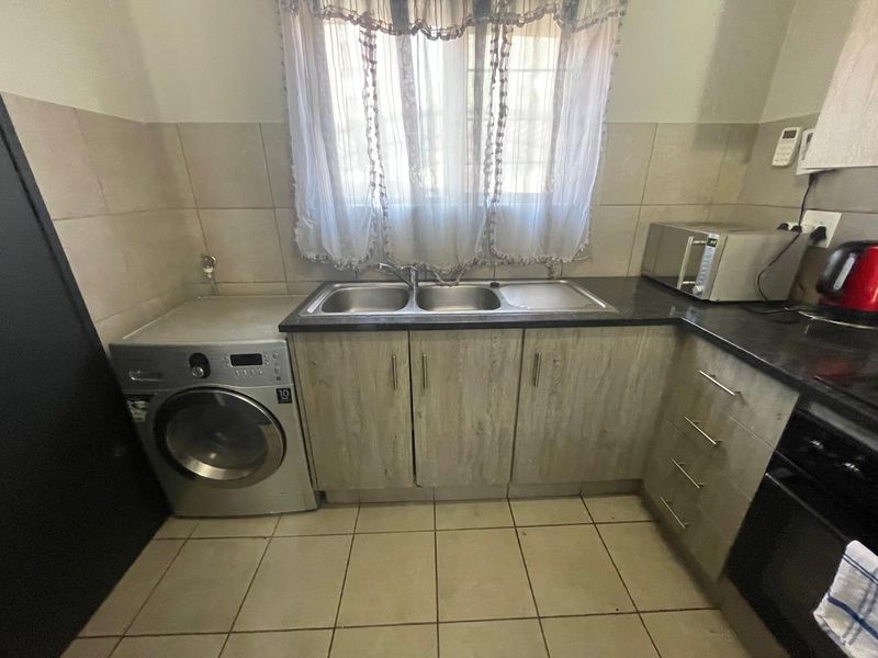 Functional kitchen featuring laminate cabinetry, stone countertops, double bowl sink, and integrated space for a washing machine with tiled splashbacks.