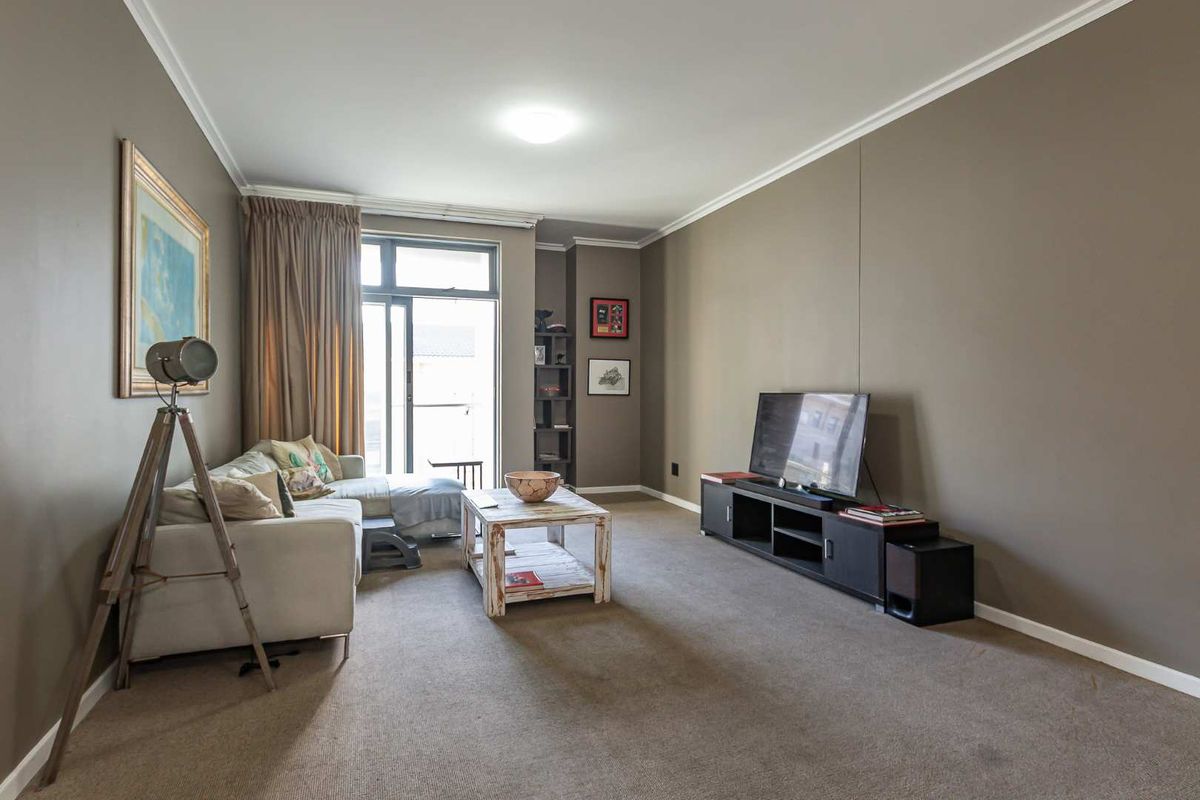 A living room featuring neutral wall tones, carpeted flooring, and a sliding glass door providing access to a balcony.