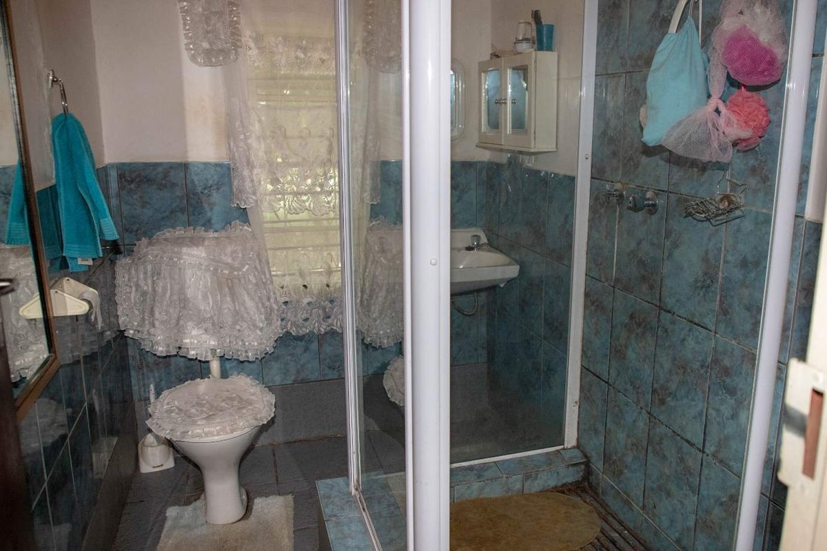 A dated bathroom featuring a shower enclosure, wall-mounted basin, and toilet with blue tiled finishes, offering significant potential for modernization and renovation.
