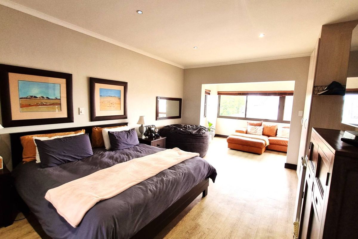 Spacious bedroom featuring laminate flooring, recessed downlighting, and built-in storage, with an integrated seating area by the window.