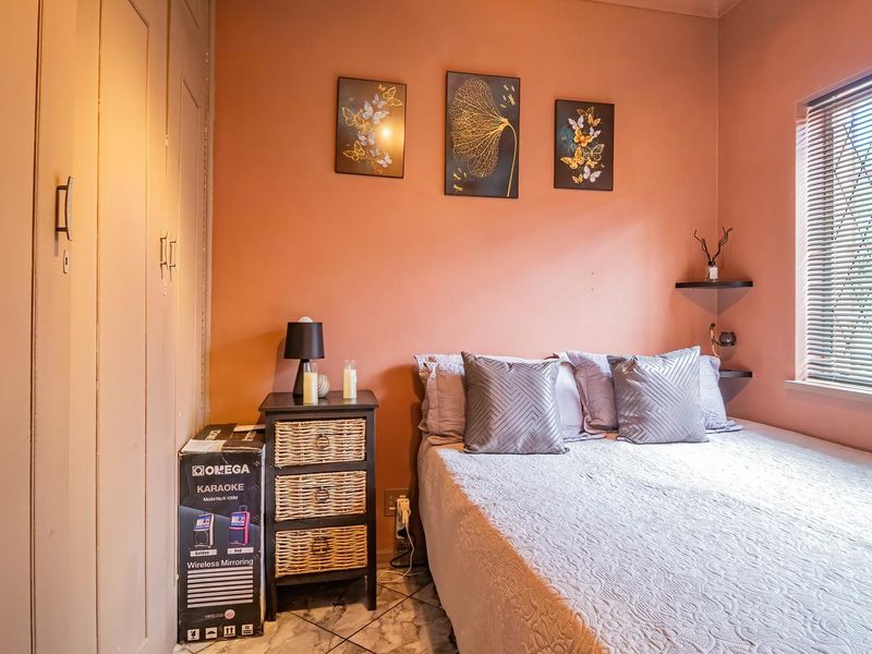 A cozy bedroom featuring built-in cupboards, tiled flooring, and a window fitted with security bars, providing a functional and private sleeping space.
