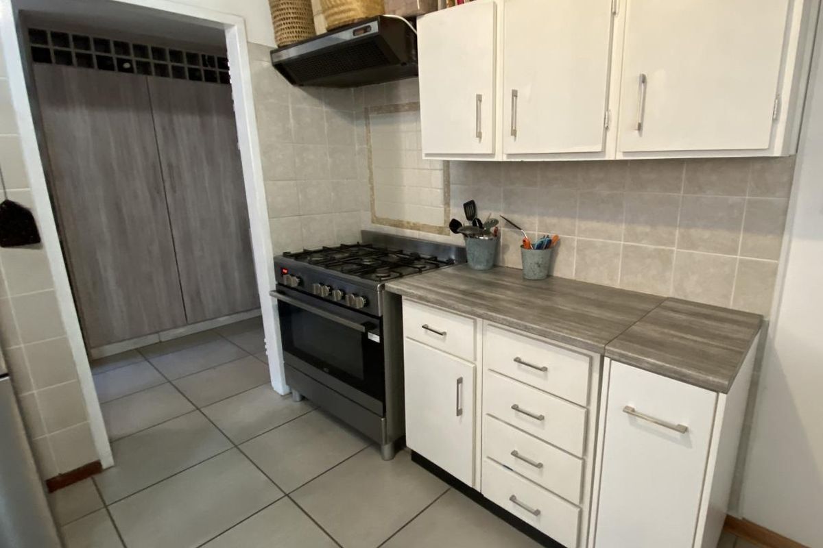 A functional kitchen featuring white cabinetry, laminate countertops, a gas stove with extractor fan, and tiled flooring, with an adjacent scullery area.