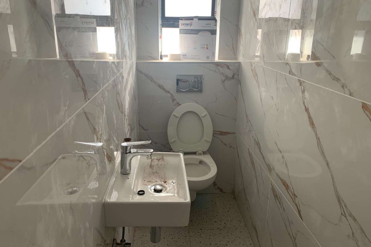 A compact bathroom featuring marble-effect wall tiling, a wall-mounted washbasin, and a modern concealed-cistern toilet.