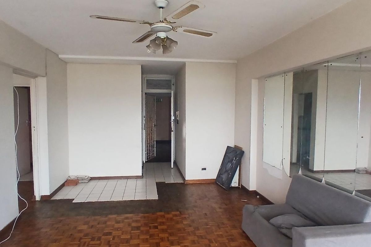 Spacious living area featuring parquet flooring, a ceiling fan, and large wall-mounted mirrors, offering a blank canvas for renovation and modernization.