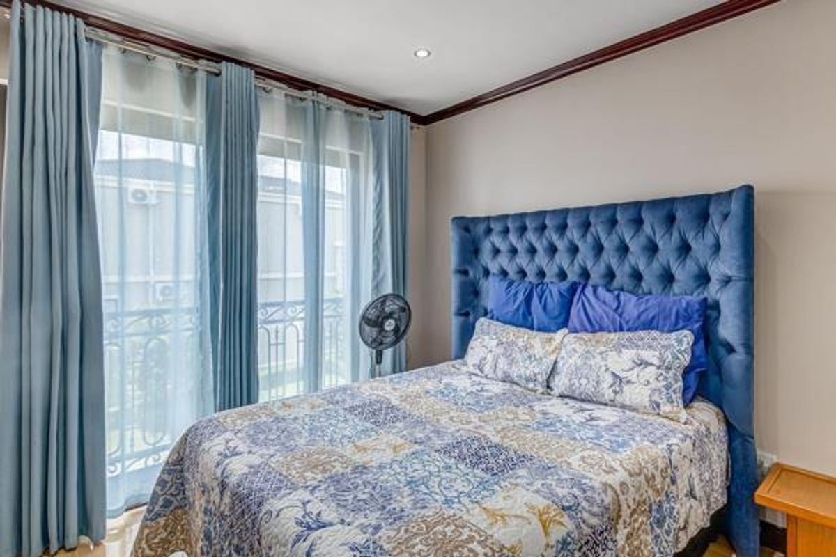 A well-lit bedroom featuring a large window with access to a balcony, finished with crown molding and neutral wall tones.