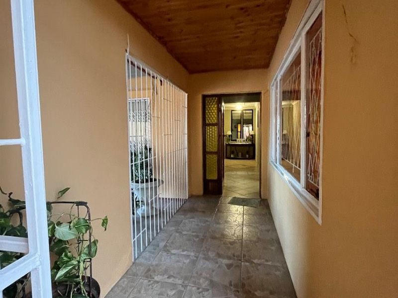 A covered outdoor patio area featuring tiled flooring, a timber ceiling, and security bars on the windows and side enclosure.