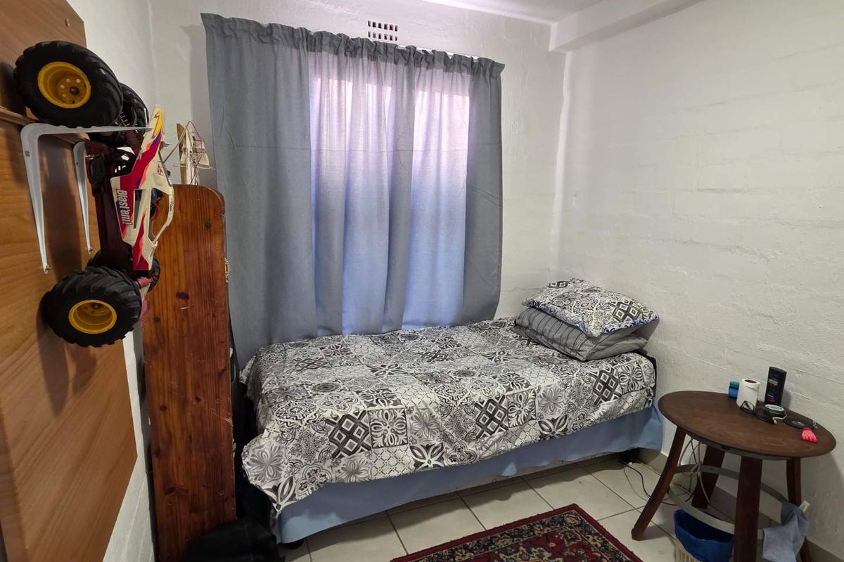 A compact bedroom featuring tiled flooring, a window with curtaining, and painted masonry walls.