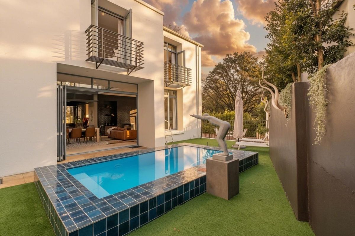 A modern rear exterior view featuring a tiled swimming pool, artificial lawn, and seamless indoor-outdoor flow through large folding glass doors.