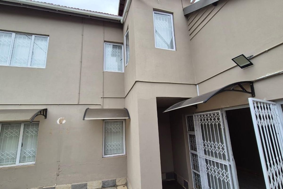 Rear elevation of a townhouse featuring security gates, window bars, and protective awnings over the entrance and windows.