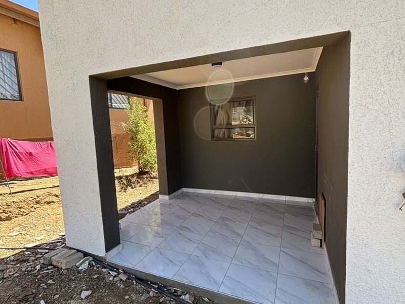 A covered patio area featuring modern marble-look floor tiles and dark accent walls, currently awaiting final landscaping and exterior finishing.