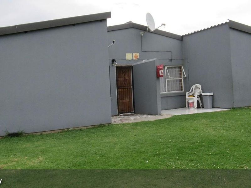 Front exterior view of a townhouse featuring a paved entrance, security gate, and satellite dish installation.