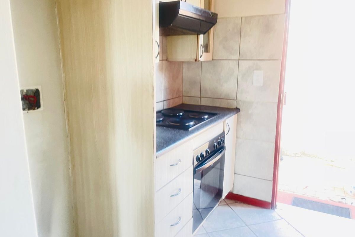 A compact kitchen area featuring built-in cabinetry, a fitted oven and hob, extractor fan, and tiled flooring with direct access to the exterior.
