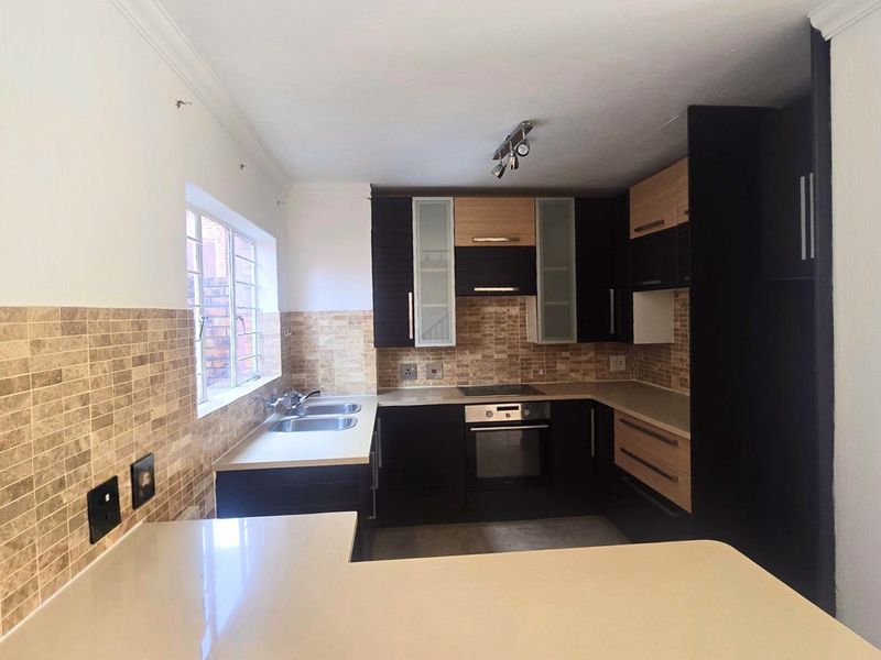 A modern, well-maintained kitchen featuring dark and wood-tone cabinetry, stone countertops, a built-in oven, electric hob, and a double basin sink.