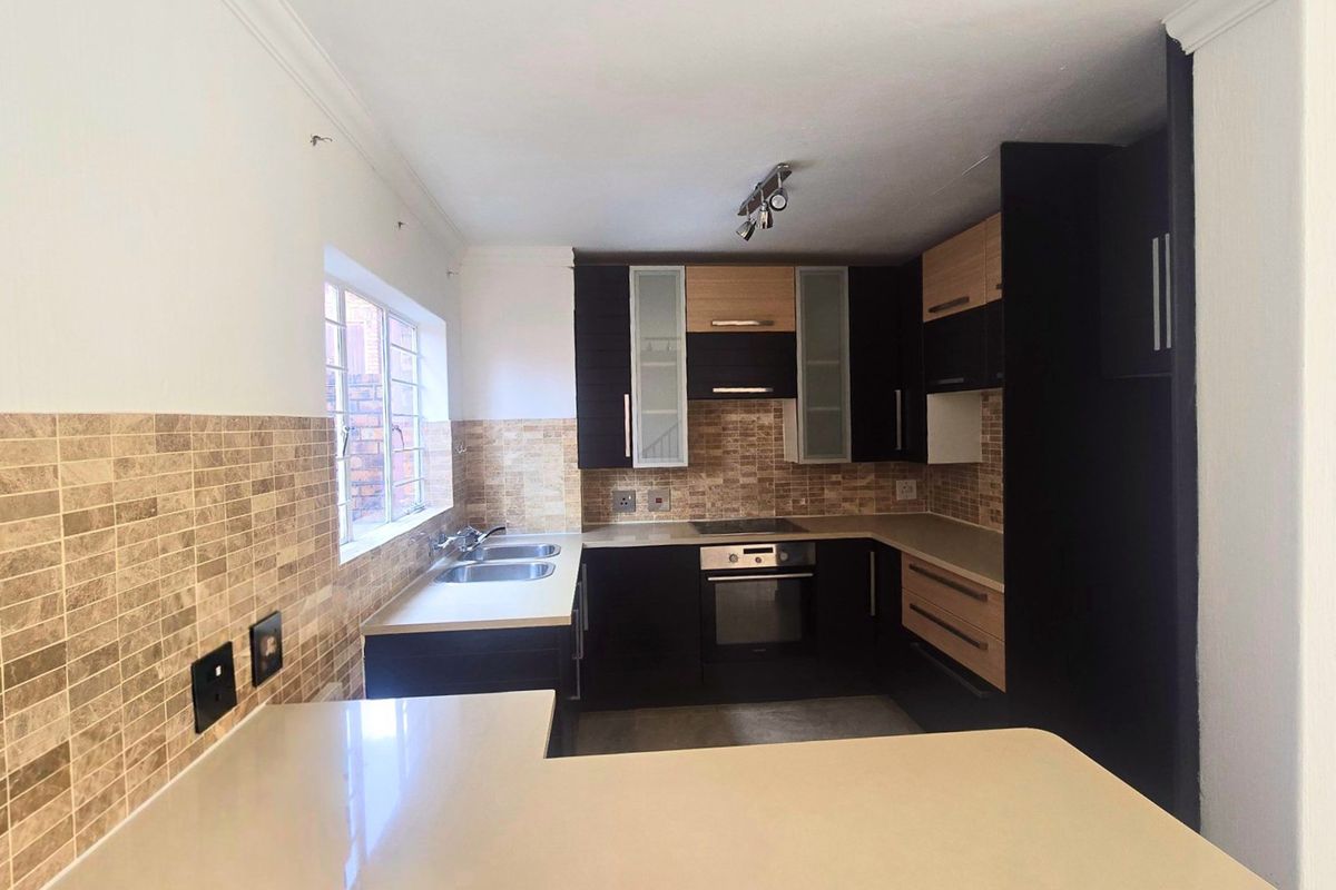 A modern, well-maintained kitchen featuring dark and wood-tone cabinetry, stone countertops, a built-in oven, electric hob, and a double basin sink.