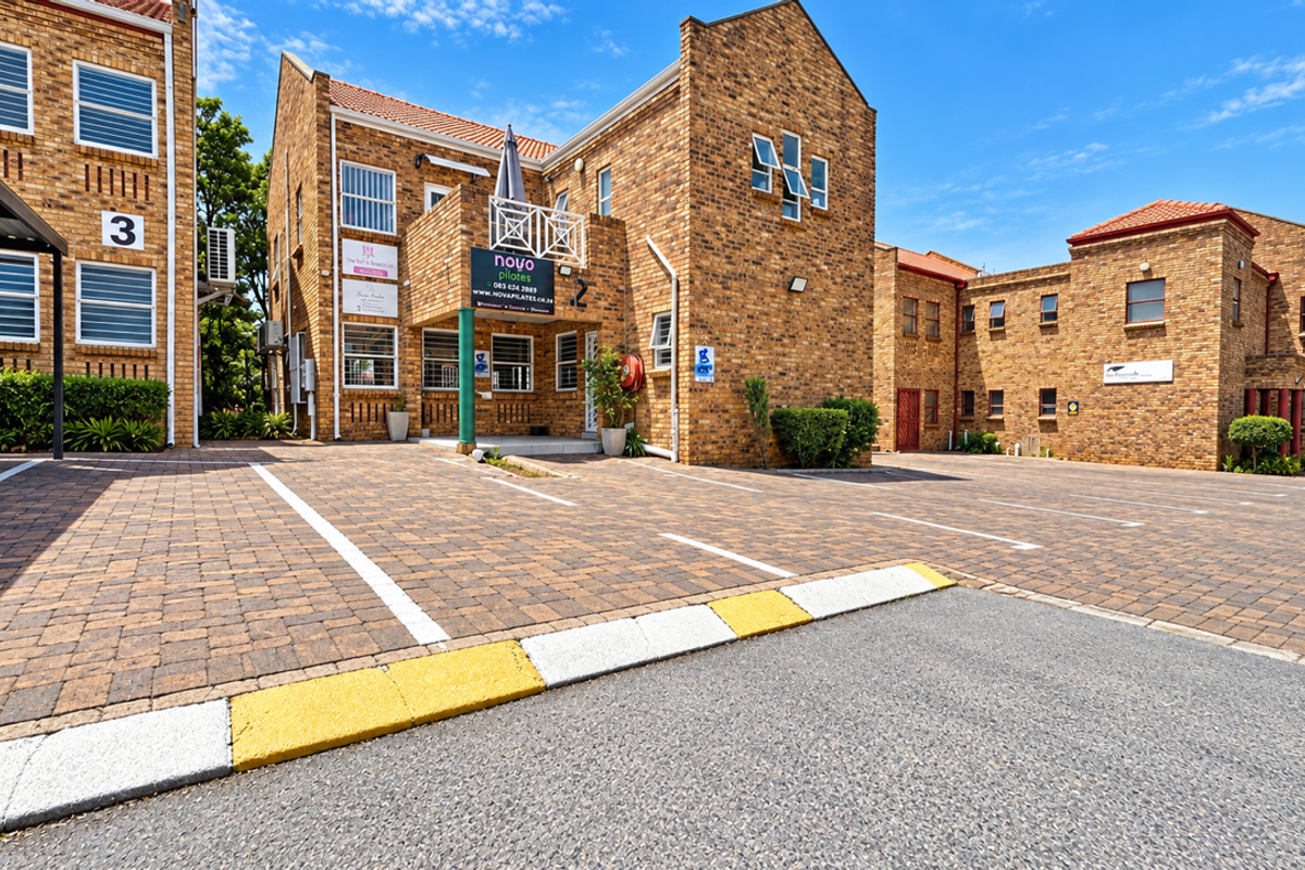 Exterior view of a multi-unit commercial brick building featuring a paved parking lot, covered parking bays, and prominent business signage.