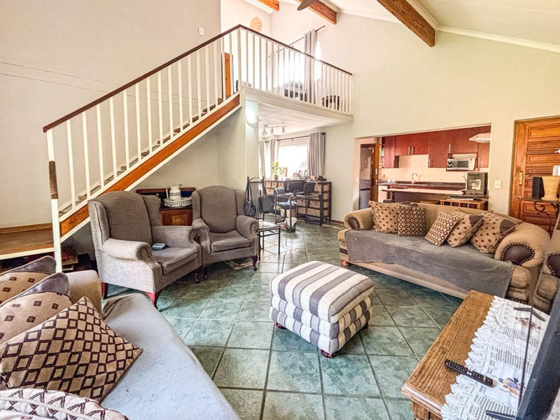 Spacious open-plan living area featuring a mezzanine level, exposed timber beams, tiled flooring, and an integrated kitchen space with built-in cabinetry.