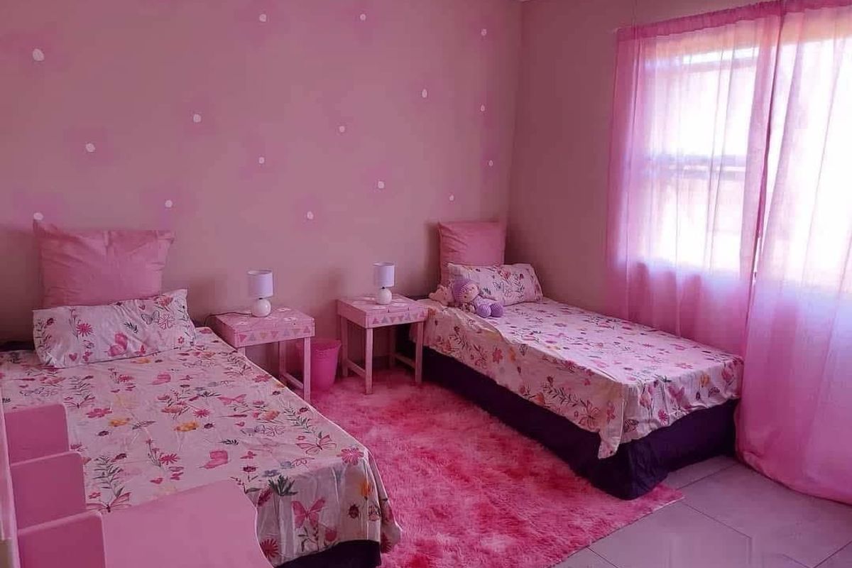 A bedroom featuring tiled flooring and a window with sheer curtains, currently styled with a pink theme.