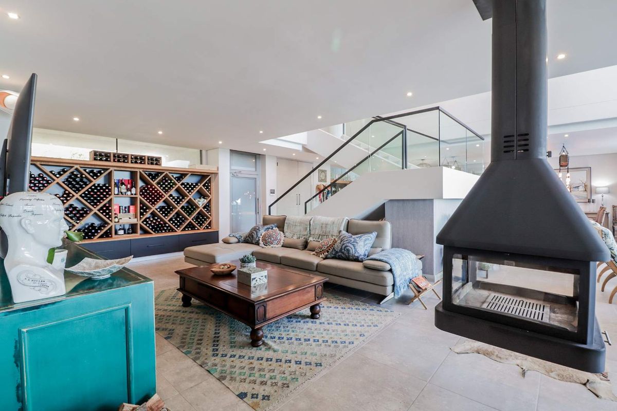 Spacious open-plan living area featuring a modern suspended fireplace, custom built-in wine storage, and a contemporary staircase with glass balustrades.
