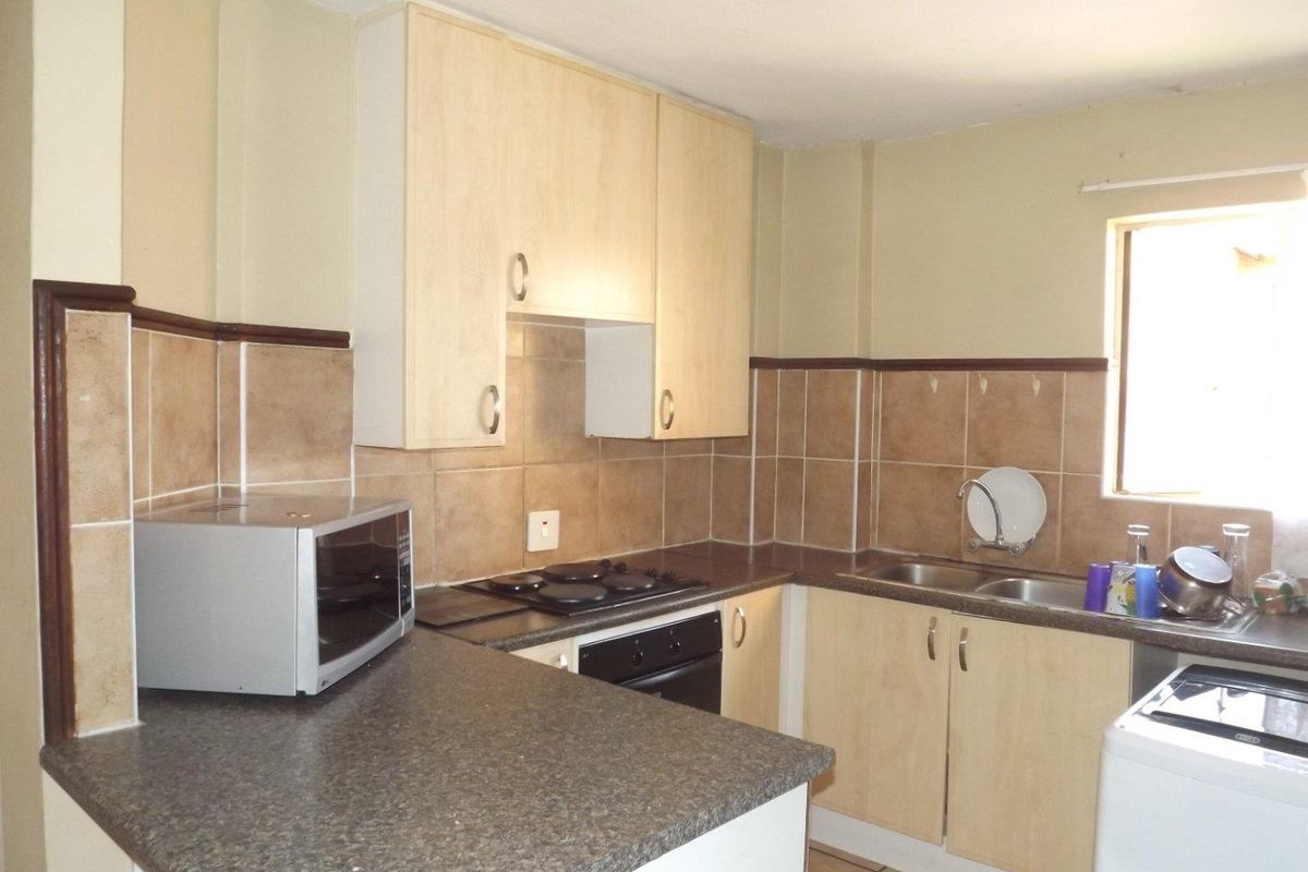 Functional kitchen featuring laminate cabinetry, stone-look countertops, built-in oven and hob, and tiled splashbacks with a double bowl sink.