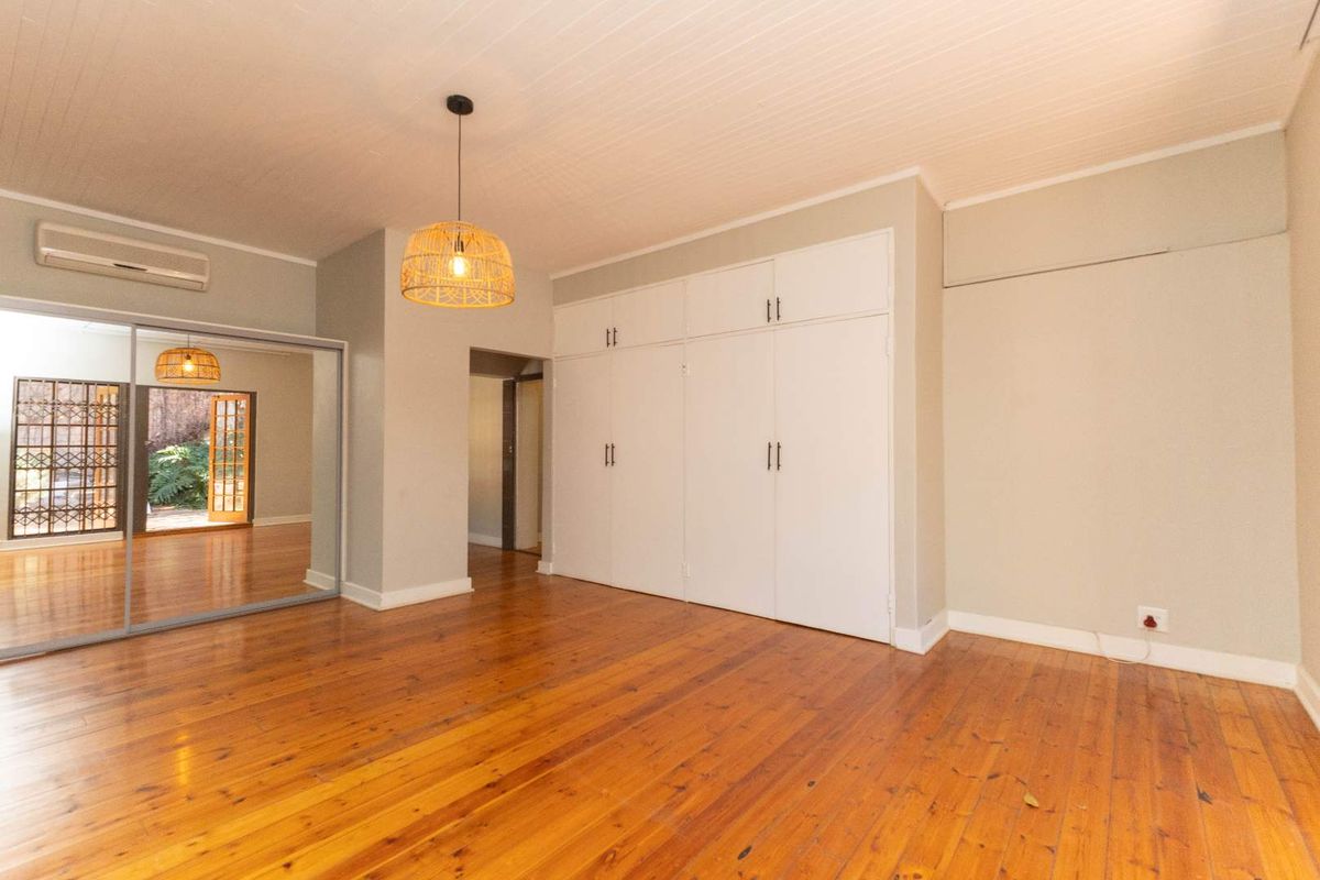 Spacious bedroom featuring polished timber flooring, built-in cabinetry, and a wall-mounted air conditioning unit.