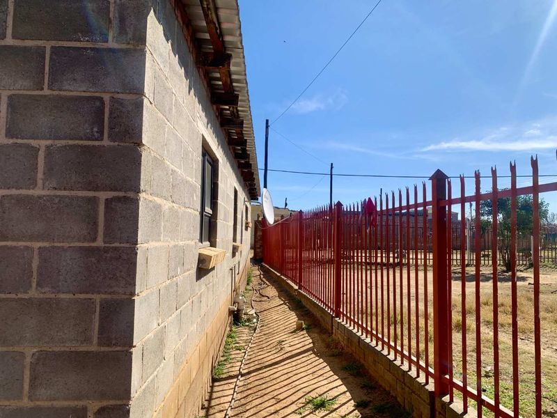 Side exterior view of the property featuring unfinished concrete block walls, a corrugated metal roof, and secure metal palisade perimeter fencing.