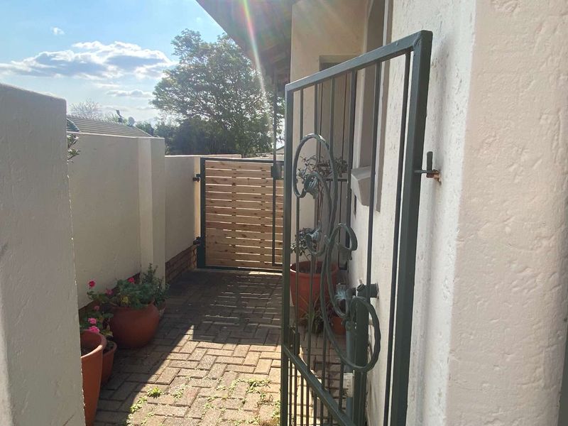 A private entrance walkway featuring a decorative wrought iron gate, a timber slat gate, and paved flooring leading to the townhouse entrance.